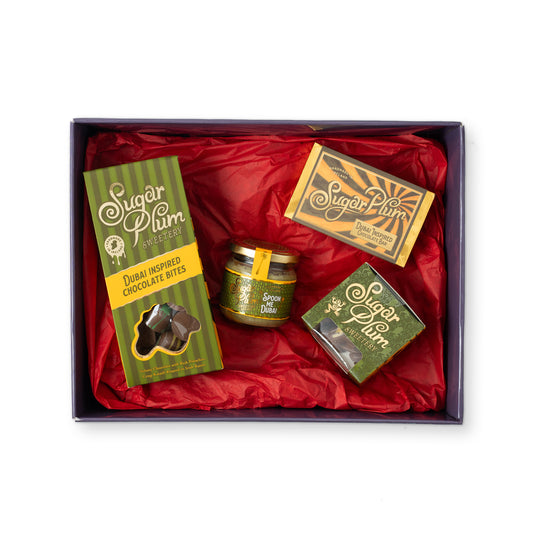 A Sugar Plum Sweet Treats gift box filled with red tissue paper, containing a green package of chocolate bites, a small jar of sweets, and two decorated boxes.