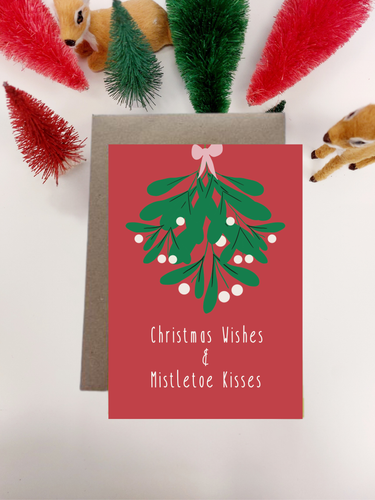 Irish Made Red Christmas card with mistletoe design and text, surrounded by festive decorations on a light background.